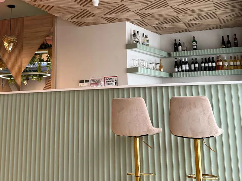 Nowoczesna lada barowa OiKO z dekoracyjnymi miętowymi panelami i ażurowym drewnianym sufitem w stylowej restauracji.