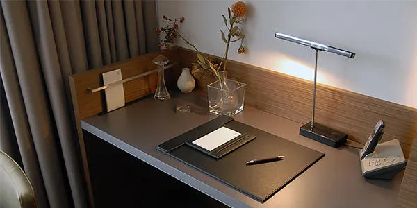 Spójny system mebli hotelowych OiKO: biurko i zabudowa łóżka wykonane z trwałych materiałów premium w nowoczesnym pokoju hotelowym.