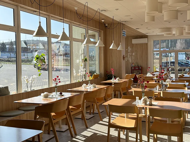Kompleksowe wyposażenie restauracji przez OiKO: drewniane stoły i krzesła w jasnym, przeszklonym wnętrzu o nowoczesnym designie.